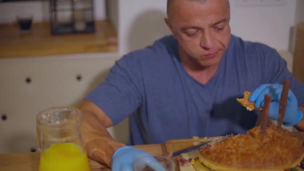 レストランのテーブルで手袋でハンバーガーを食べている大人のはげ男 フォーカスがシフト — ストック動画