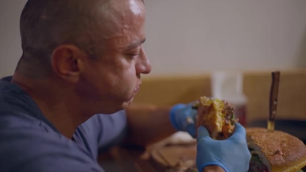 Volwassen Kale Man Eet Een Stuk Sappige Hamburger Met Handschoenen — Stockvideo
