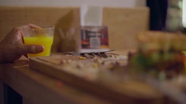 一块开胃的汉堡包放在木板上 一只手拿着一杯橙汁 — 图库视频影像