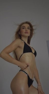 Sahne arkasında uzun saçlı güzel bir fitness modelinin beyaz arka planda dikey video formatında çekimi. Mükemmel bikini şekli.