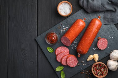 Baharatlı, soslu ve fesleğenli siyah arka planda sosis. Üst görünüm, yatay.