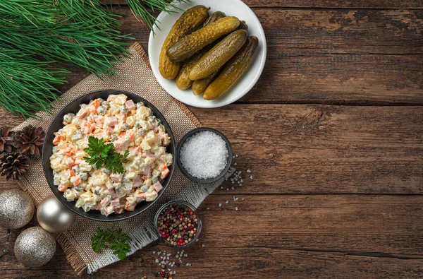 Festive olivier salad, pickled cucumbers and fir decorations on a wooden background. — Stock Photo, Image