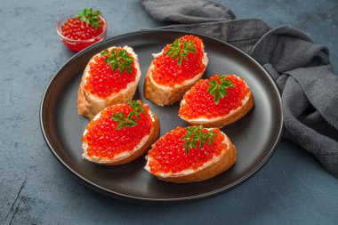 Siyah bir tabakta kırmızı havyarlı, tereyağlı ve maydanozlu sandviçler..