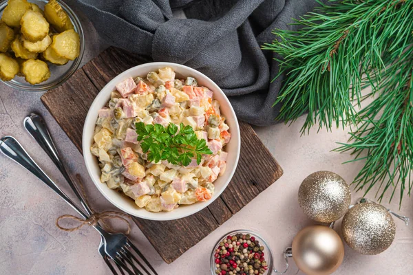 Traditional olivier salad of finely chopped vegetables and sausage on the background of Christmas decorations. — Stock Photo, Image