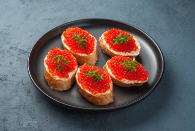 Siyah bir arka planda kırmızı havyarlı, tereyağlı ve maydanozlu sandviçler. Yan görünüm, yatay.