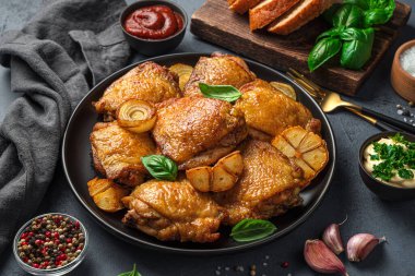 Kızarmış tavuk butları, sarımsak, soğan ve siyah arka planda siyah bir tabakta taze fesleğen. Yan görünüm, yakın plan.