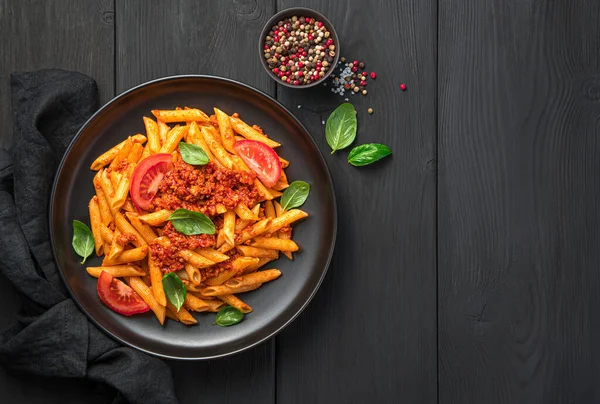 トマトと肉のボロネーゼソースと黒の背景に新鮮なバジルとペンパスタ 伝統的なイタリア料理 トップビュー コピースペース — ストック写真