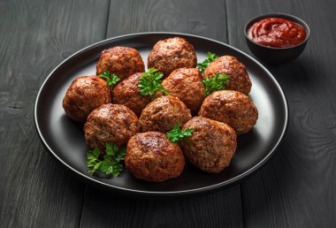 Kızarmış köfteler siyah bir tabakta yakın planda domates soslu koyu bir arka planda. Yan görünüm.