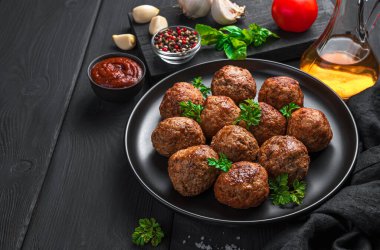 Siyah bir tabakta, soslu ve baharatlı fesleğen köftesi. Yan görünüm, boşluk kopyala.