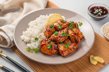 Teriyaki tavuğu, pilav ve bej bir tabakta taze otlar. Geleneksel bir Japon yemeği. Yan görünüm, yakın plan.