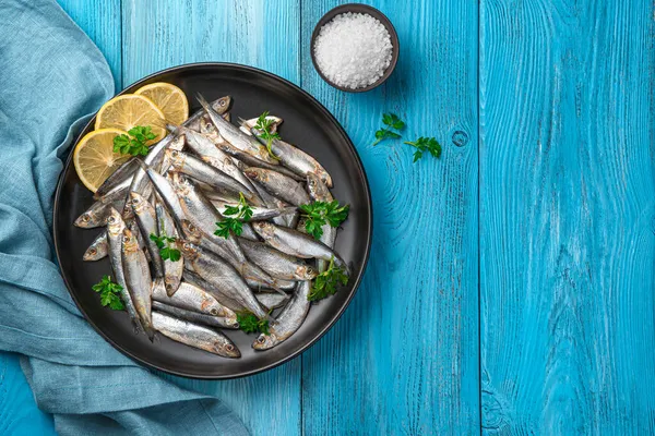 Mavi arka planda limon ve maydanozlu siyah bir tabakta serpiştir. Üst görünüm, alanı kopyala.