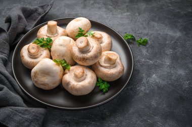Koyu arkaplanda taze şampiyonlar ve maydanozlu bir tabak. Yan görünüm, yatay.
