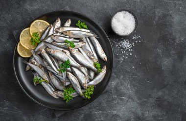 Koyu arkaplanda limon ve maydanozla dolu bir tabak. Üst görünüm, alanı kopyala.