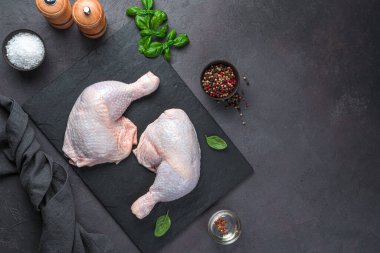 Koyu arkaplanda baharatlı ve fesleğenli çiğ tavuk bacağı. Üst görünüm, alanı kopyala.