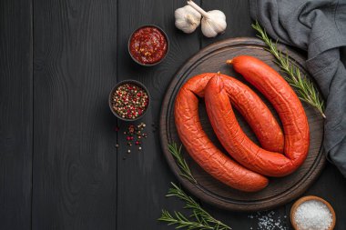 Biberiyeli füme Krakow sosisi ve siyah ahşap arka planda kesme tahtasındaki sos halkaları. Üst görünüm, alanı kopyala.