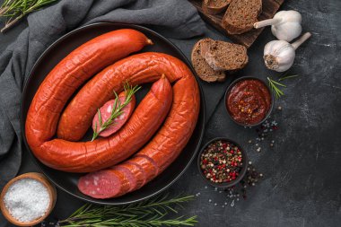 Sos, baharat ve koyu arkaplanda taze biberiye ile tütsülenmiş Krakow sosisi. Üst görünüm, alanı kopyala.