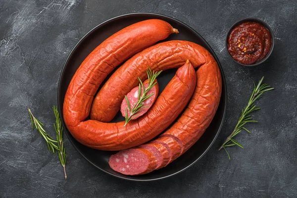 Arka planda biberiye ve domates soslu bir tabak füme sosis. Üst görünüm, yakın çekim.