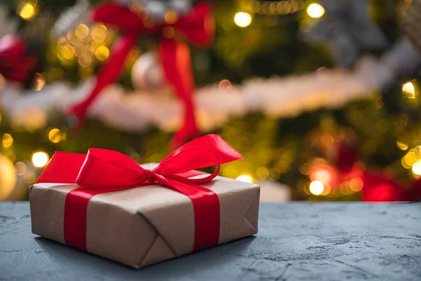 Noel ağacının arka planında kırmızı kurdele olan bir hediye. Noel arkaplanı. Yan görüş, kopyalama alanı. Seçici odak.