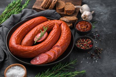 Smoked sausage with sliced on a dark background with bread, sauce and rosemary.