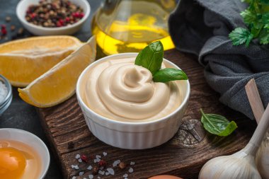 Mayonnaise with fresh basil and ingredients on a dark background. Homemade mayonnaise, close-up.