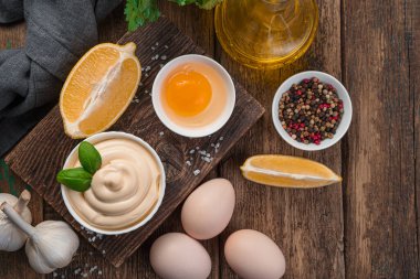 Ingredients for mayonnaise and the sauce itself in a white bowl on a wooden background. Top view, copy space.