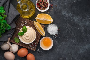 Mayonnaise in a white bowl and ingredients for its preparation on a dark background. Top view, copy space.
