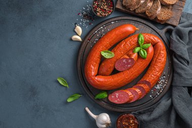 Smoked sausage with sliced basil and garlic on a dark background. Krakow sausage. Top view, copy space.