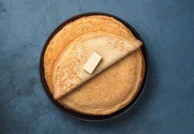 Fried pancakes with butter on a dark gray-blue background. Maslenitsa, Russian blini. Top view, copy space.
