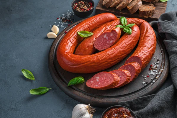 Rings of Krakow smoked sausage with basil and spices on a dark background. Side view, copy space
