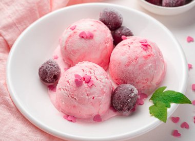 Donmuş kirazlı üç top dondurma ve beyaz tabakta kalpler. Yan görünüm, yakın plan.