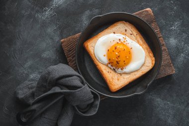 Koyu bir arka planda kızartma tavasında sahanda yumurtalı kahvaltı. Yağda yumurtalı ekmek. Üst görünüm.