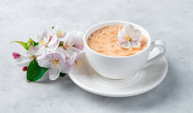 Bir kapuçino bardağı ve gri arka planda çiçek açan bir dal. Zarif çiçek arkaplanı. Yan görünüm.