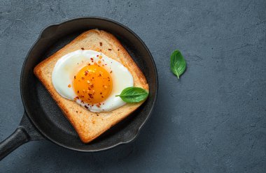 Kavrulmuş yumurta, biberli ve fesleğenli tost kızartma tavasında grafit arka planda..