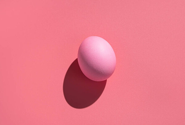 Розовое яйцо на розовом фоне с твёрдой тенью. Абстрактный пасхальный фон.