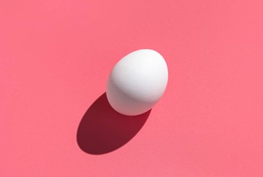 Pembe arka planda sert gölgesi olan beyaz bir yumurta. Paskalya, asgari gıda konsepti.