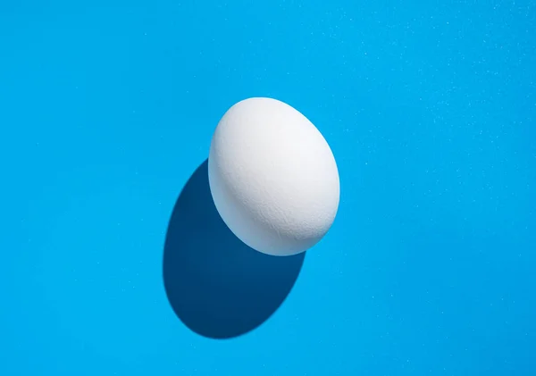 Białe Jajko Niebieskim Tle Twardym Cieniem Koncepcja Wielkanocnej Minimalistycznej Żywności — Zdjęcie stockowe