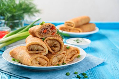 Doldurulmuş krep, et ve havuçla birlikte mavi arka planda ekşi krema. Geleneksel Rus krepleri. Yan görünüm, boşluk kopyala.
