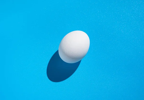 Białe Jajko Niebieskim Tle Twardym Cieniem Minimalistyczne Odżywianie Streszczenie Kontekstu — Zdjęcie stockowe