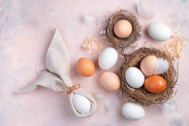 Açık pembe arka planda bir yuvada peçete ve yumurtadan yapılmış Paskalya tavşanı. Mutlu Paskalyalar konsepti. Üst görünüm.