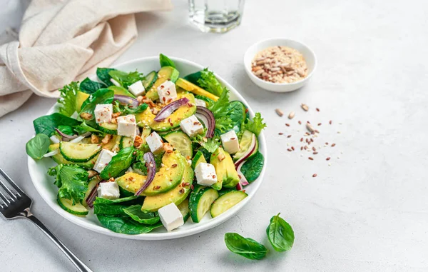 Avocado salad with cucumbers, feta and nuts on a gray background. Side view, copy space.