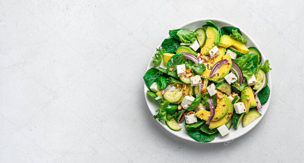 Avocado salad with fresh herbs, feta, cucumber and seeds on a light gray background.