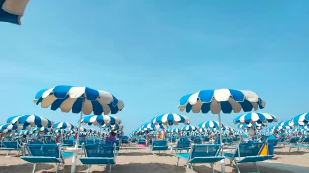 Weiße und blaue Sonnenschirme, die vom Wind am Strand verweht werden — Stockvideo