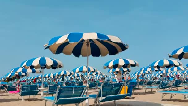 Weiße und blaue Sonnenschirme, die vom Wind am Strand verweht werden — Stockvideo
