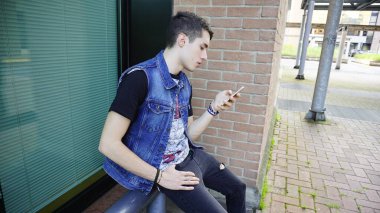 Kot ceketli yakışıklı çocuk akıllı telefon kullanıyor, yüksek kalite fotoğraf.