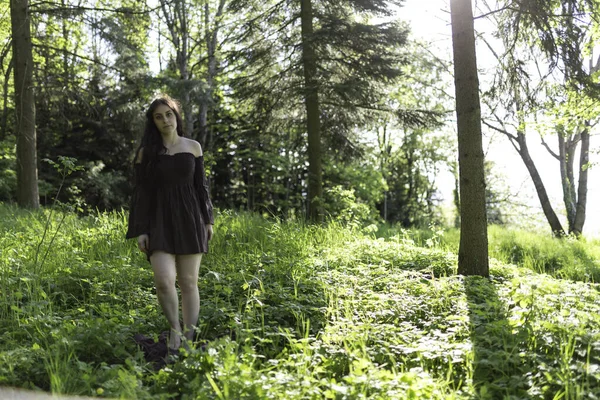 Güzel kız kısa kahverengi elbiseyle ormanda yalınayak yürüyor. Yüksek kalite fotoğraf