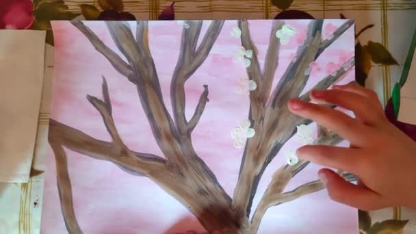 child draws flowers and trees on paper with fingers