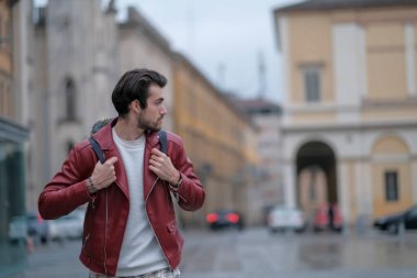 Reggio Emilia 'nın ortasında kırmızı deri ceketli ve sırt çantalı güzel bir adam. Yüksek kalite fotoğraf