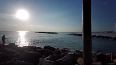 Rimini Akdeniz 'de gün batımında kayalıklardaki balıkçı.