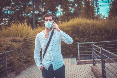 Güzel, koyu renk saçlı bir İtalyan çocuk. Telefonda virüs maskesi takıyor. Yüksek kalite fotoğraf