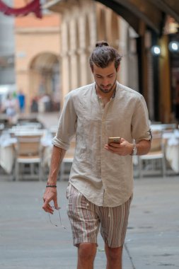 Güzel, siyah saçlı İtalyan çocuk yürüyor ve cep telefonuna bakıyor. Yüksek kalite fotoğraf